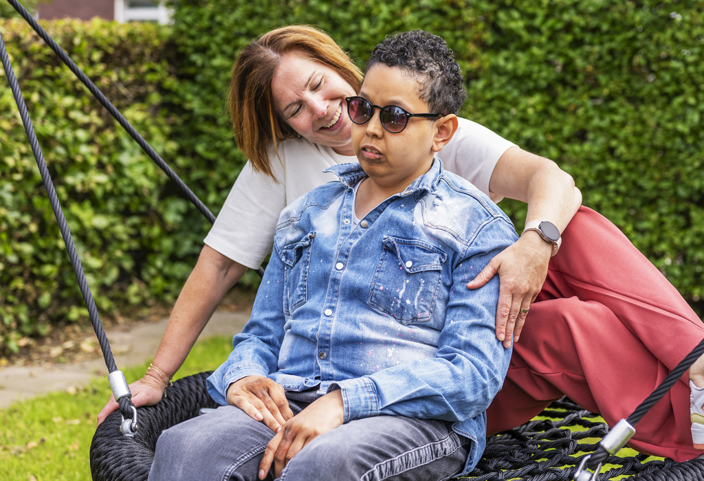 Een coördinerend cliëntbegeleider zit op een schommel met een blinde vrouw. De vrouw draagt een zonnebril.