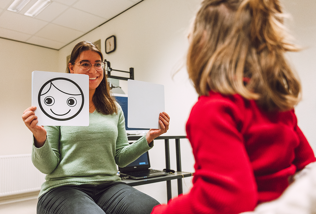Orthoptist voert een oogtest uit bij een kind, en wijst op afbeeldingen met twee beelden