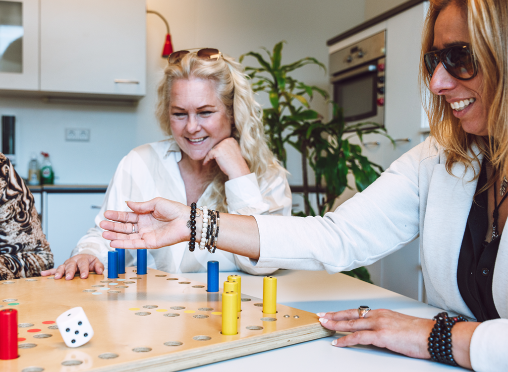 Twee vrouwen spelen een aangepast bordspel. De dobbelsteen en pionnen zijn extra groot.
