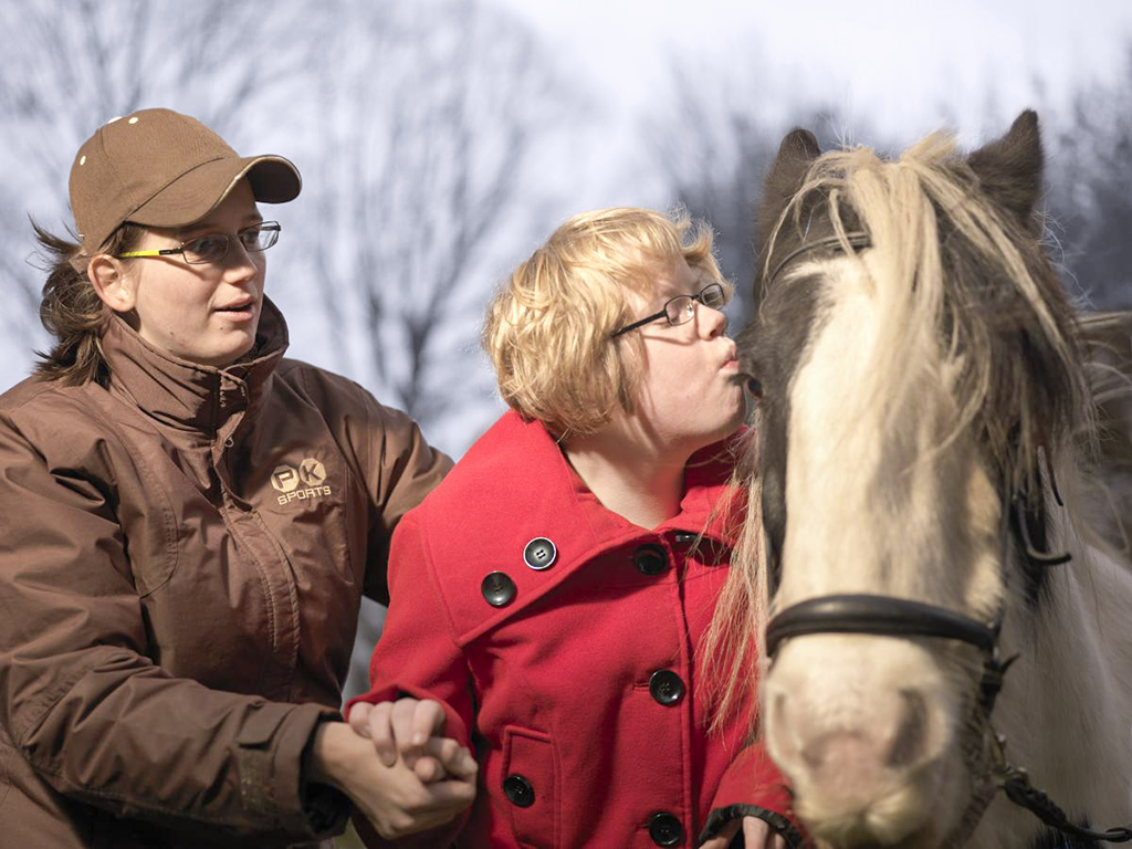 Een vrijwilliger helpt een meisje terwijl zij een paard knuffelt