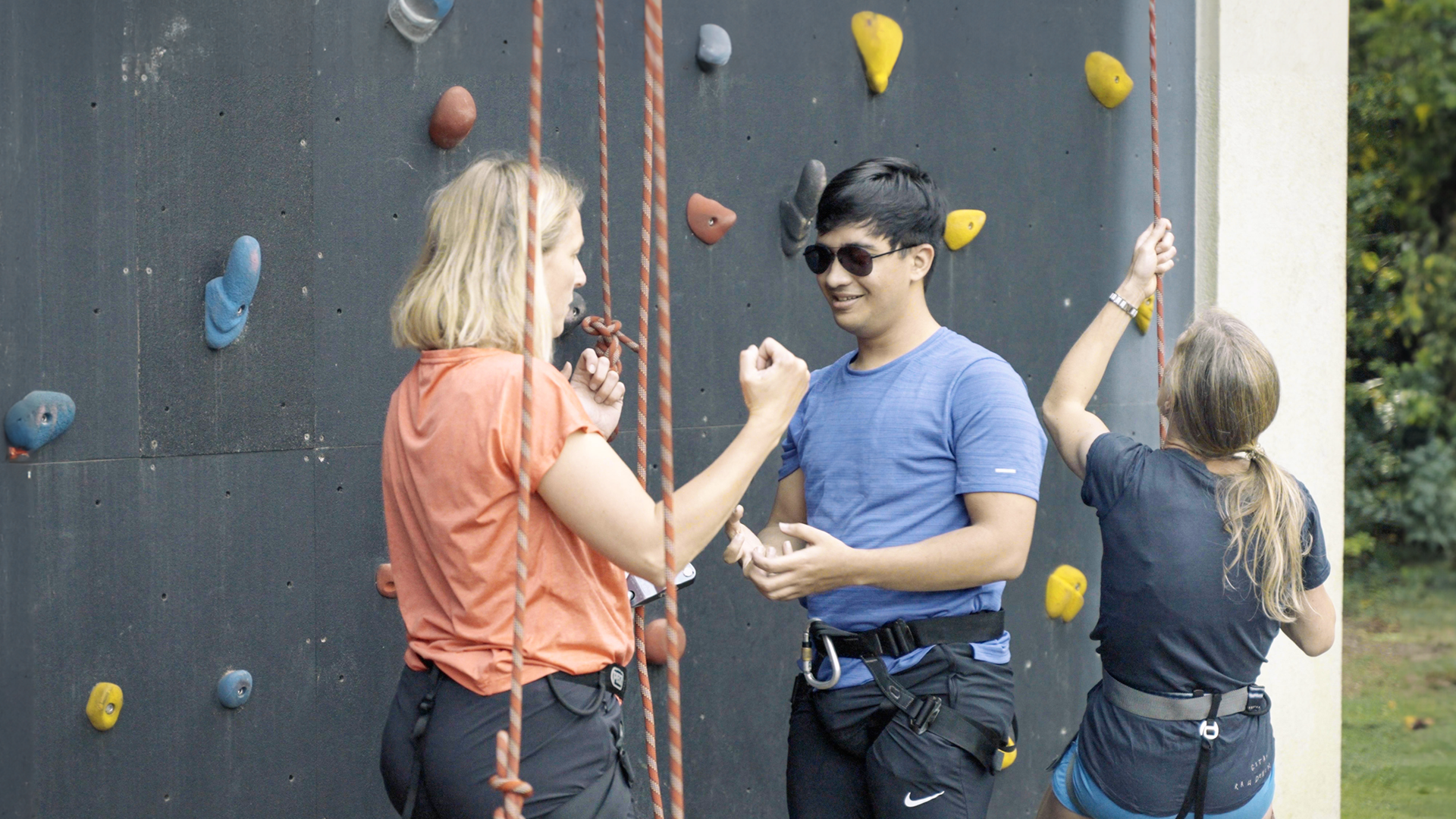 Een bewegingsagoog en een jongen met een visuele beperking staan klaar bij een klimwand op de intensieve revalidatie locatie Visio het Loo-erf