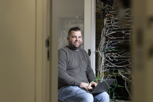 Een ICT-Technisch er zit in een kast met kabels op zijn laptop.