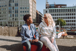 Een maatschappelijk werker zit met een slechtziende vrouw buiten in Rotterdam naan de haven.