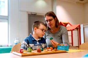 Een Onderwijsassistent laat een jonge leerling een plastic (tastbare) broccoli zien.