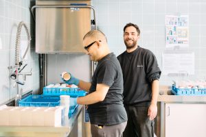 Een begeleider staat met een client in een spoelkeuken. De client doet de afwas.