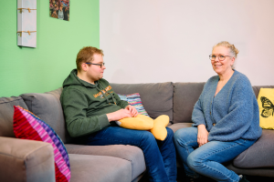 Een ambulant begeleidster zit samen met een client op de bank in de huiskamer.