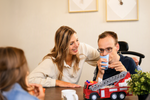Een begeleidster lacht naar een jongen die in een rolstoel zit. Hij drinkt uit een beker.